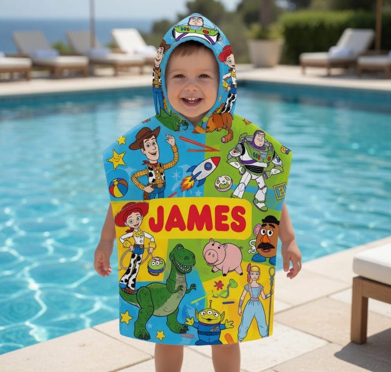 Puede incluir: Un ni&ntilde;o con una toalla con capucha azul, verde y amarilla con personajes de la pel&iacute;cula Toy Story. La toalla tiene el nombre "JAMES" impreso en letras rojas. El fondo muestra una piscina y tumbonas.