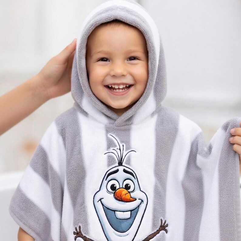 May include: A hooded child's towel featuring a smiling Olaf from Frozen. The towel is white with gray stripes and a gray hood. The Olaf graphic is centered on the chest. The child is smiling.