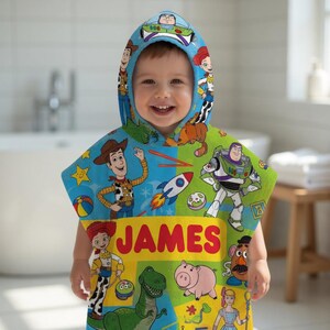 Puede incluir: Una toalla con capucha y colorida con personajes de la pel&iacute;cula Toy Story. La toalla es azul y verde con im&aacute;genes de Woody, Buzz Lightyear y otros personajes. El nombre "JAMES" est&aacute; impreso en la parte delantera.