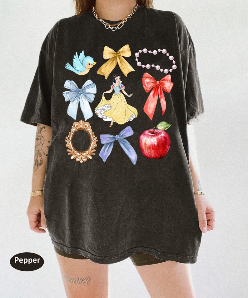 K&ouml;nnte beinhalten: Schwarzes Oversize-T-Shirt mit einem grafischen Druck von Schneewittchen, einem roten Apfel, einem blauen Vogel, einem Spiegel und mehreren Schleifen.