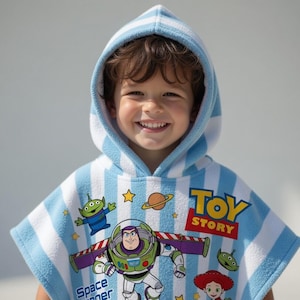May include: A child wearing a blue and white striped hooded towel featuring characters from the Toy Story movie. The towel has images of Buzz Lightyear, an alien, and the words "Toy Story".