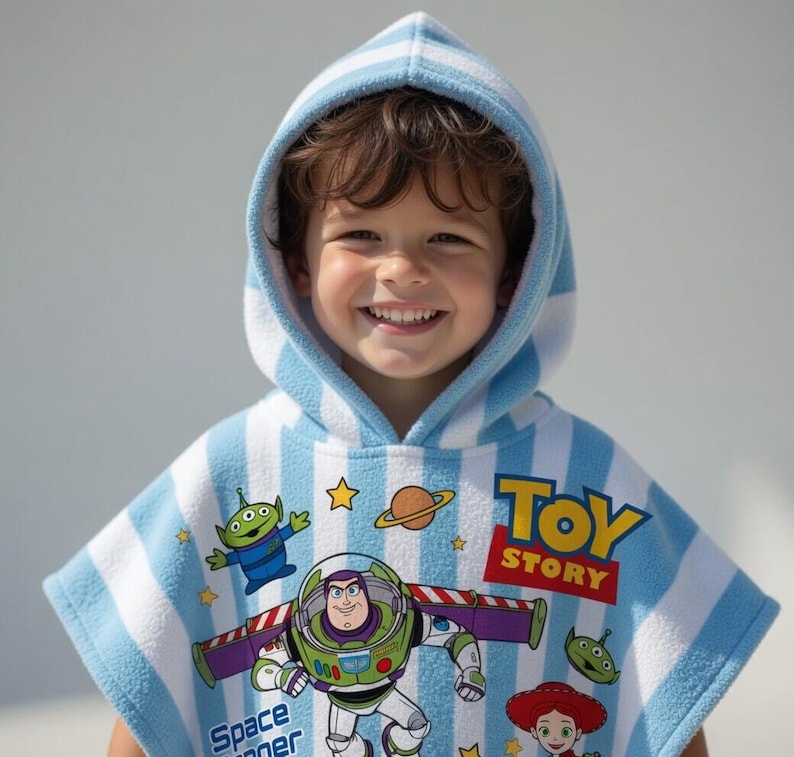May include: A child wearing a blue and white striped hooded towel featuring characters from the Toy Story movie. The towel has images of Buzz Lightyear, an alien, and the words "Toy Story".