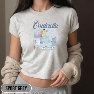 May include: A light gray t-shirt with a graphic of Cinderella and Prince Charming dancing. The text "Cinderella is a wish your heart makes" is printed on the shirt.