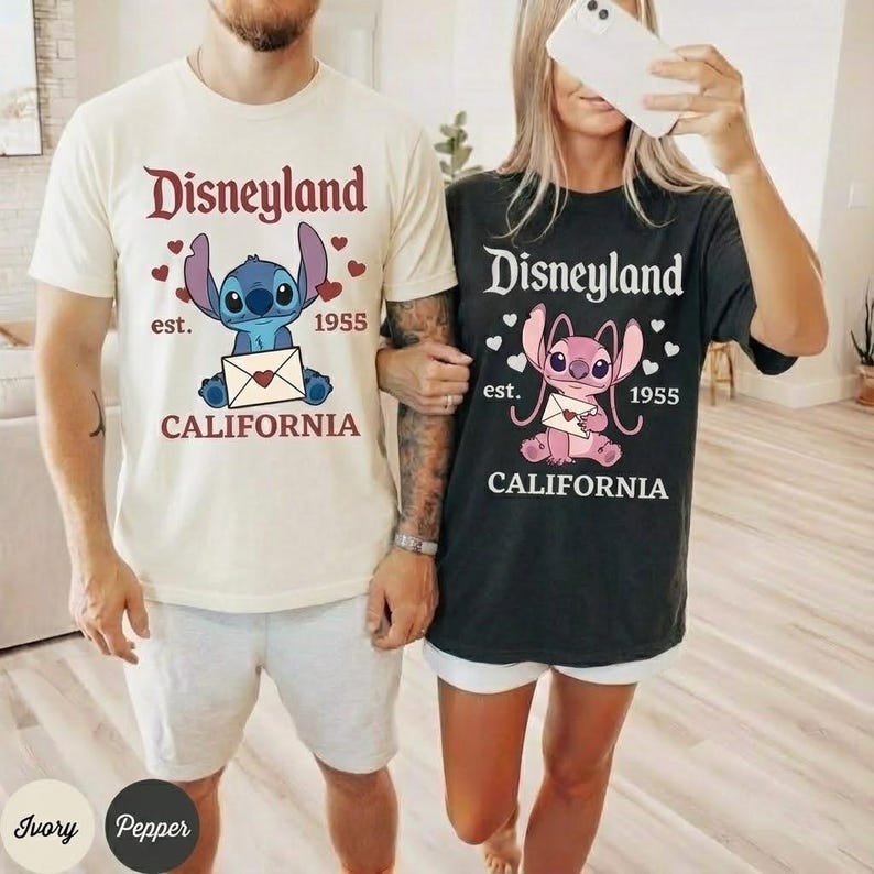 Op de afbeelding: Twee T-shirts, &eacute;&eacute;n ivoorkleurig en &eacute;&eacute;n zwart, met een Disneyland-ontwerp. Het ontwerp bevat het woord "Disneyland", het personage Stitch of Angel, de tekst "est. 1955" en "CALIFORNIA".