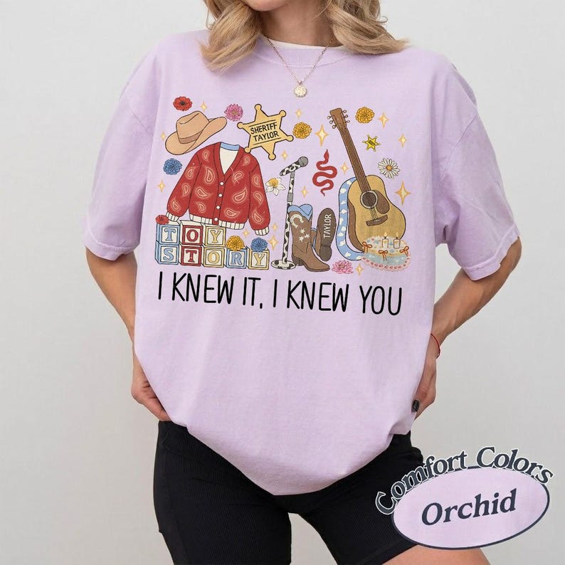 May include: A light purple t-shirt featuring a graphic print with a cowboy hat, a red paisley cardigan, a sheriff badge labeled Sheriff Taylor, a microphone, a brown cowboy boot, a guitar, and blocks spelling Toy Story. Text reads I KNEW IT, I KNEW YOU.