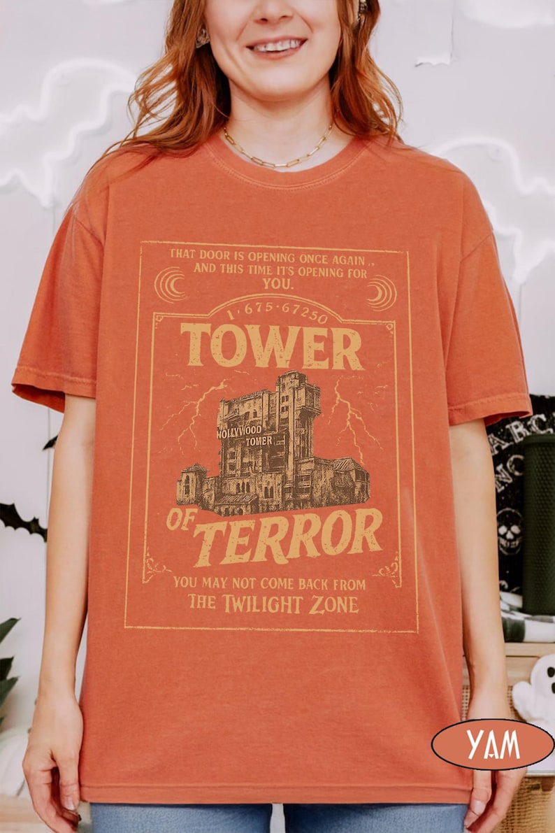 May include: Orange short-sleeved t-shirt with a vintage graphic of the Hollywood Tower of Terror. The graphic includes the text "TOWER OF TERROR" and other phrases. The shirt is a solid orange colour.