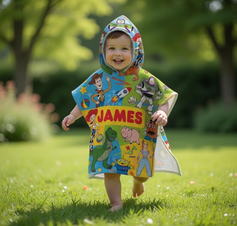Puede incluir: Un ni&ntilde;o con un poncho con capucha colorido con personajes de Toy Story. El poncho es principalmente azul, verde y amarillo, con el nombre "JAMES" impreso en letras rojas. El ni&ntilde;o sonr&iacute;e y camina sobre hierba verde.