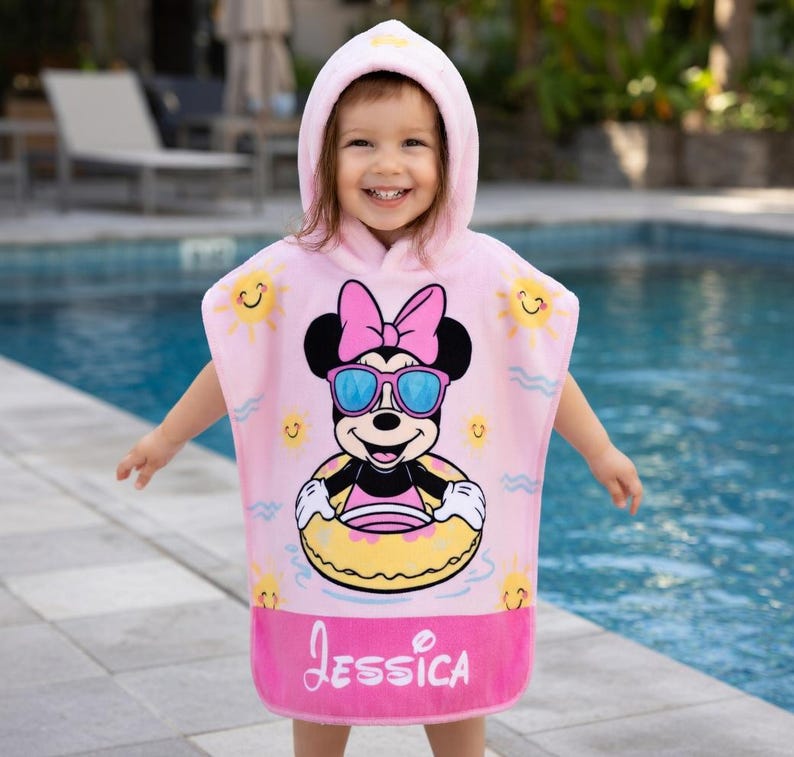 May include: Pink hooded beach towel featuring Minnie Mouse wearing sunglasses and a pink bow. The towel has a yellow inner tube, sun graphics, and the name "Jessica" in pink script.