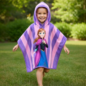 Puede incluir: Poncho con capucha para ni&ntilde;os, a rayas moradas y rosas, con un personaje impreso. El poncho lo lleva un ni&ntilde;o al aire libre, sobre un c&eacute;sped verde, con &aacute;rboles al fondo.