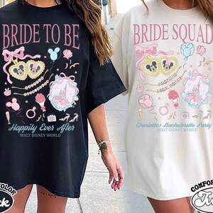 Può includere: T-shirt neri e avorio Comfort Color con grafica a tema Disney. La maglietta nera dice "Bride to Be" e "Happily Ever After". La maglietta avorio dice "Bride Squad" e "Charlotte's Bachelorette Party".