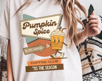 May include: Off-white t-shirt with a vintage graphic design. The image shows a sign that says "Pumpkin Spice", a cartoon coffee cup, and the phrases "All Day, Every Day" and "'Tis The Season".