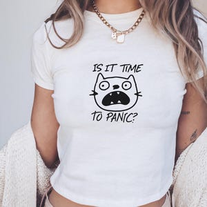 Könnte beinhalten: Weißes, bauchfreies T-Shirt mit einer schwarz-weißen Illustration einer Katze mit dem Text "Is it time to panic?"