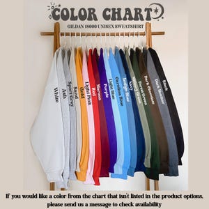 May include: A color chart for Gildan 18000 unisex sweatshirts, displaying a range of colors including white, ash, sport grey, and black. The chart includes text that says "COLOR CHART" and "GILDAN 18000 UNISEX SWEATSHIRT".