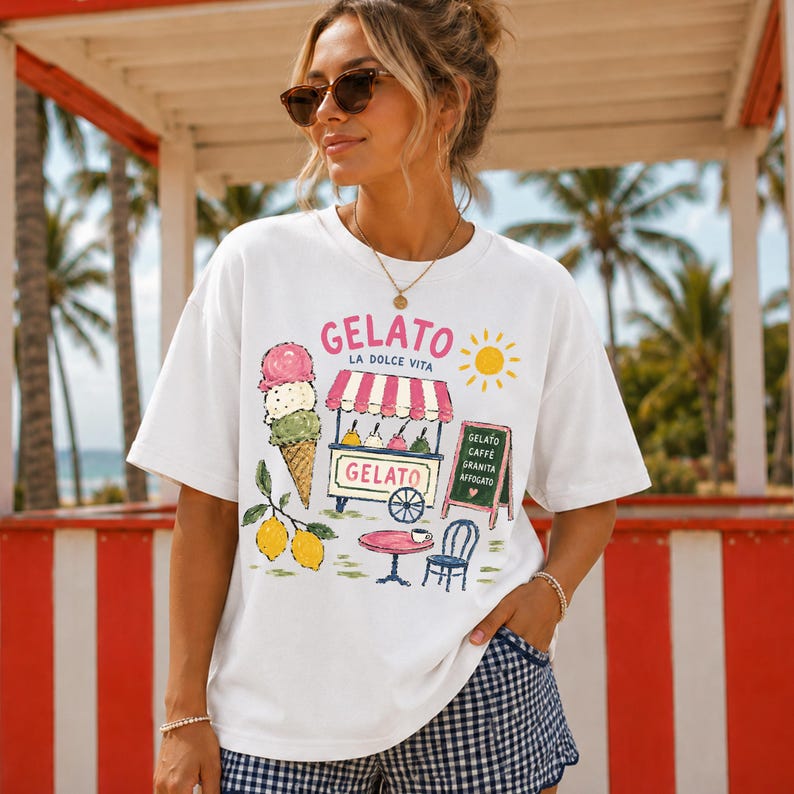 Puede incluir: Camiseta blanca con un dise&ntilde;o de helado colorido. El gr&aacute;fico incluye un cono de helado, un carrito de helados, limones y las palabras "Gelato La Dolce Vita". Un peque&ntilde;o letrero enumera los sabores de helado. La persona lleva gafas de sol.