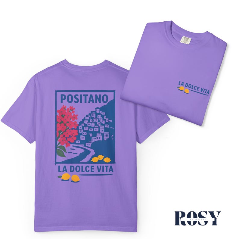 May include: Two lavender t-shirts. One displays a graphic of Positano, Italy, with red flowers, white buildings, and yellow lemons. The text "LA DOLCE VITA" and "POSITANO" are also visible. The second shirt shows the text "LA DOLCE VITA" and two lemons.
