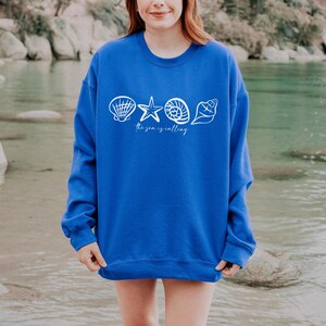 May include: A royal blue sweatshirt with a white graphic of seashells, a starfish, and the text "The sea is calling".
