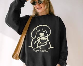 May include: Black sweatshirt with a cream-colored illustration of a dog holding a coffee cup. The text "Coffee Weather" is below the dog. The sweatshirt has long sleeves and a crew neck.