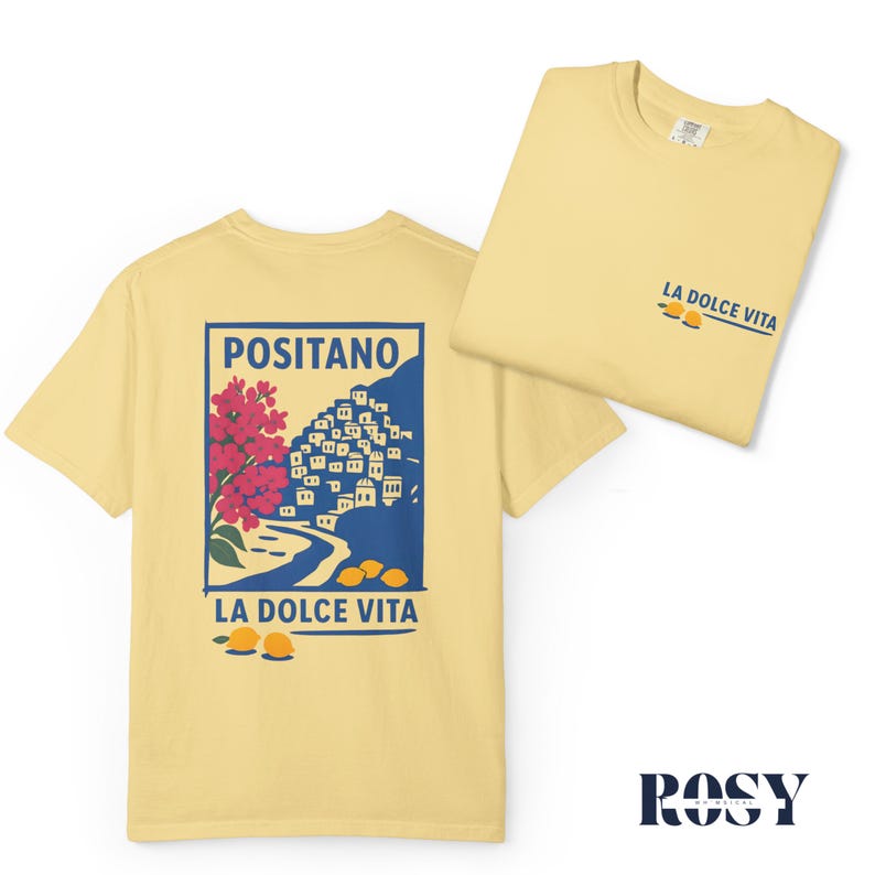 May include: Two light yellow t-shirts. One shirt features a graphic of Positano with red flowers, a blue background, and the text "LA DOLCE VITA". The other shirt has "LA DOLCE VITA" printed on the front. The brand name "ROSY" is at the bottom.