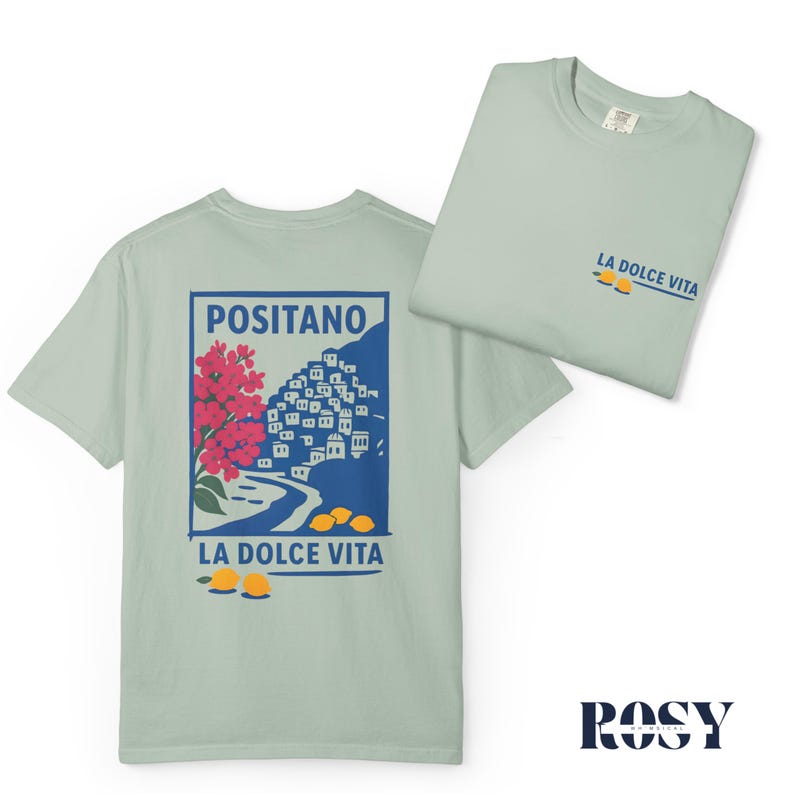 May include: Two light green t-shirts. One displays a graphic of Positano, Italy, with red flowers, blue buildings, and yellow lemons, with the text "LA DOLCE VITA." The other shirt shows the text "LA DOLCE VITA" and lemons. The brand name "ROSY" is at the bottom.
