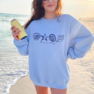 May include: Light blue sweatshirt with a graphic of seashells and a starfish. The text "The sea is calling" is printed below the graphic.