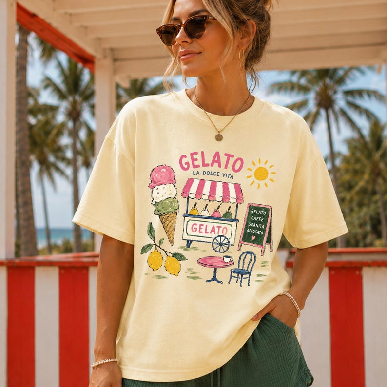 Puede incluir: Camiseta amarillo claro con un dise&ntilde;o de helado. El dise&ntilde;o incluye un cono de helado, un carrito de helado, un sol y la palabra "Gelato". La camiseta se lleva al aire libre.