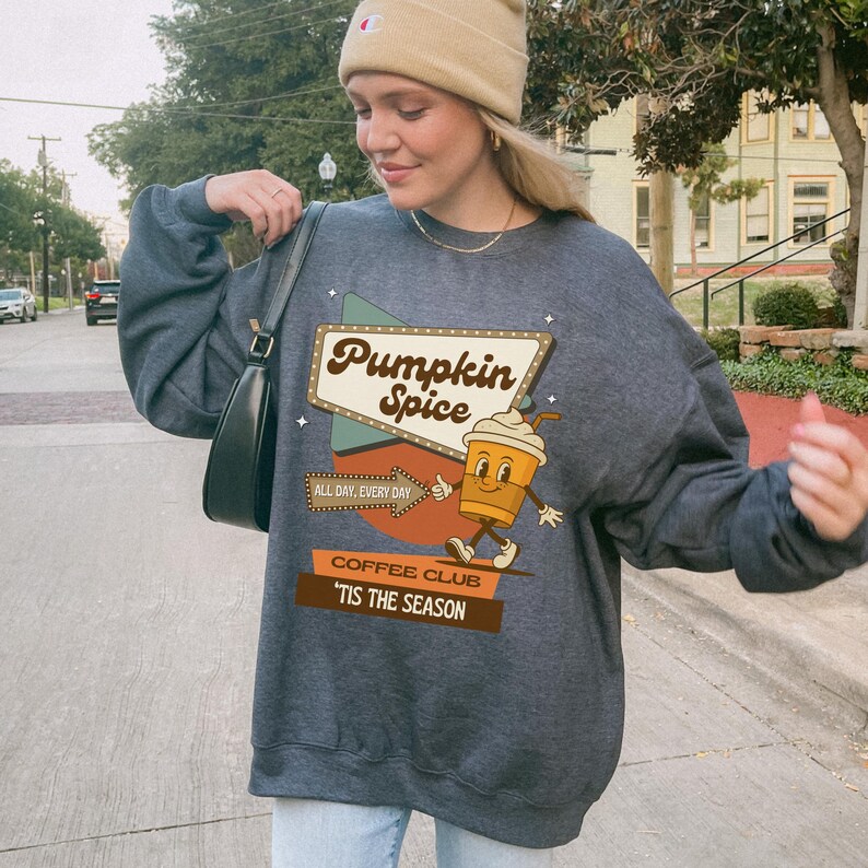 May include: Dark gray sweatshirt with a graphic that says "Pumpkin Spice" in a retro sign design. The graphic includes a cartoon coffee cup character and the text "All Day, Every Day" and "Coffee Club 'Tis The Season".