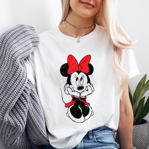 May include: White t-shirt with a black and white image of Minnie Mouse wearing a red bow. The image has a distressed look.