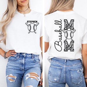 K&ouml;nnte beinhalten: Wei&szlig;es T-Shirt mit einem Baseball- und Schl&auml;ger-Design auf der Vorderseite und dem Wort "STEPHEN". Die R&uuml;ckseite des Shirts tr&auml;gt das Wort "MOM" in Leopardenmuster mit einem Baseball- und Schl&auml;ger-Design und das Wort "Baseball" vertikal geschrieben.