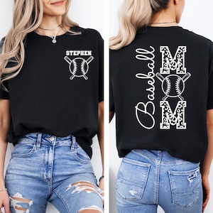 K&ouml;nnte beinhalten: Schwarzes T-Shirt mit einem wei&szlig;en Baseball- und gekreuzten Schl&auml;ger-Design auf der Vorderseite und dem Text "STEPHEN". Die R&uuml;ckseite des Shirts hat ein wei&szlig;es Design mit dem Text "Baseball MOM" mit einem Leopardenmuster.