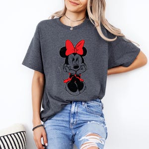 May include: A dark gray t-shirt with a cartoon image of Minnie Mouse wearing a red bow. Minnie Mouse is sitting with her arms crossed and has a red bow on her head.