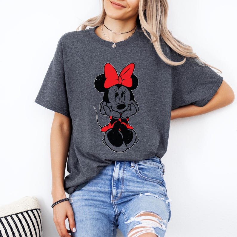 May include: A dark gray t-shirt with a cartoon image of Minnie Mouse wearing a red bow. Minnie Mouse is sitting with her arms crossed and has a red bow on her head.