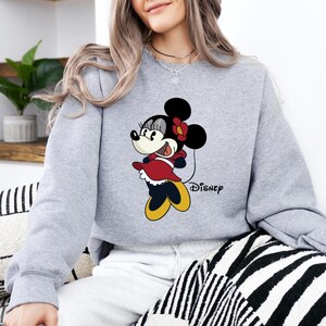 May include: A gray sweatshirt with a cartoon image of Minnie Mouse wearing a red dress and a black bow. The text "DISNEY" is printed below the image.
