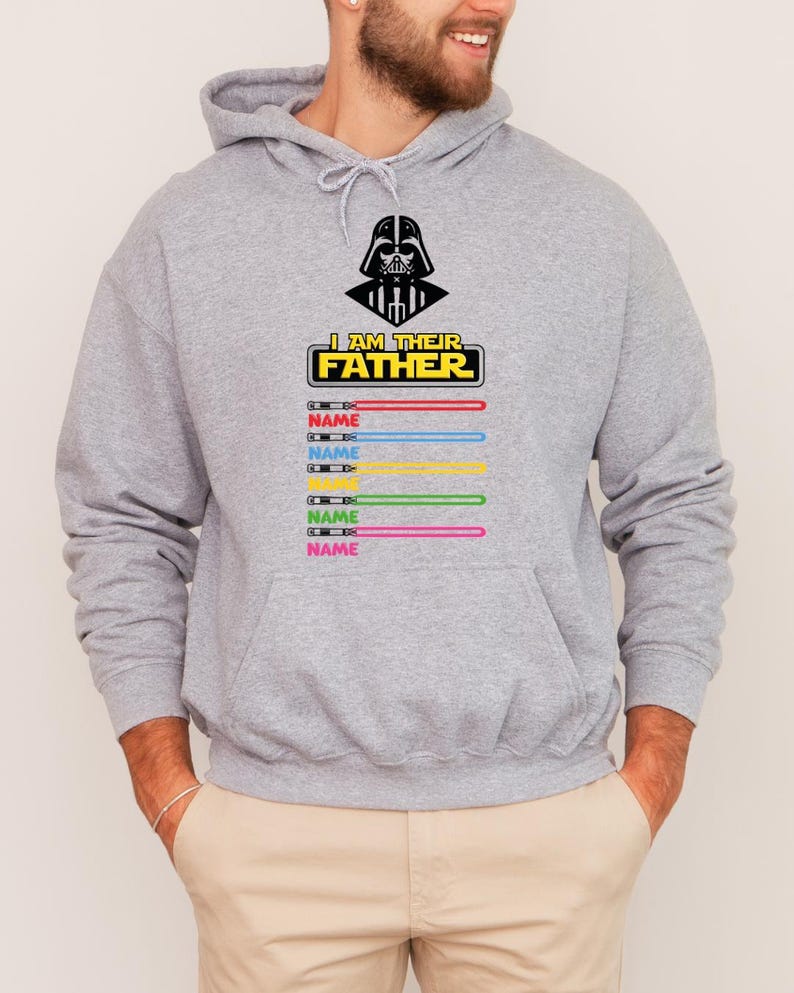 Pu&ograve; includere: Una felpa con cappuccio grigia con una grafica nera di Darth Vader e la scritta "I AM THEIR FATHER". Sotto il testo ci sono disegni di spade laser colorate con la parola "NAME" stampata su ciascuna. La felpa ha una tasca frontale.
