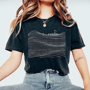 May include: Black t-shirt with a white line drawing of a boat on the ocean. The design features horizontal lines representing waves. The shirt is a dark charcoal color and has a vintage, worn look.