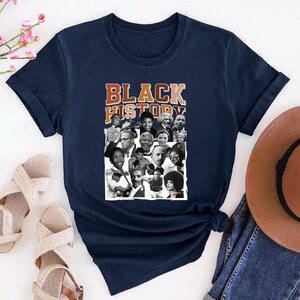 May include: A navy blue t-shirt with a collage of black and white photos of famous African Americans. The text "BLACK HISTORY" is printed in brown and orange letters on the shirt.