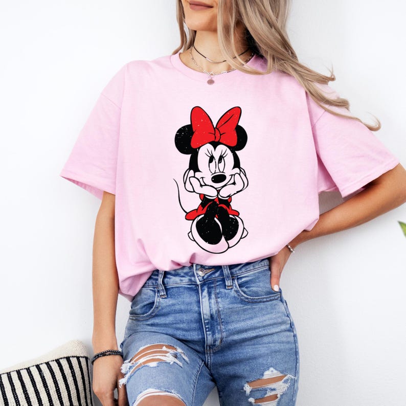 May include: A pink t-shirt with a black and white image of Minnie Mouse wearing a red bow. Minnie Mouse is sitting with her hands on her chin.