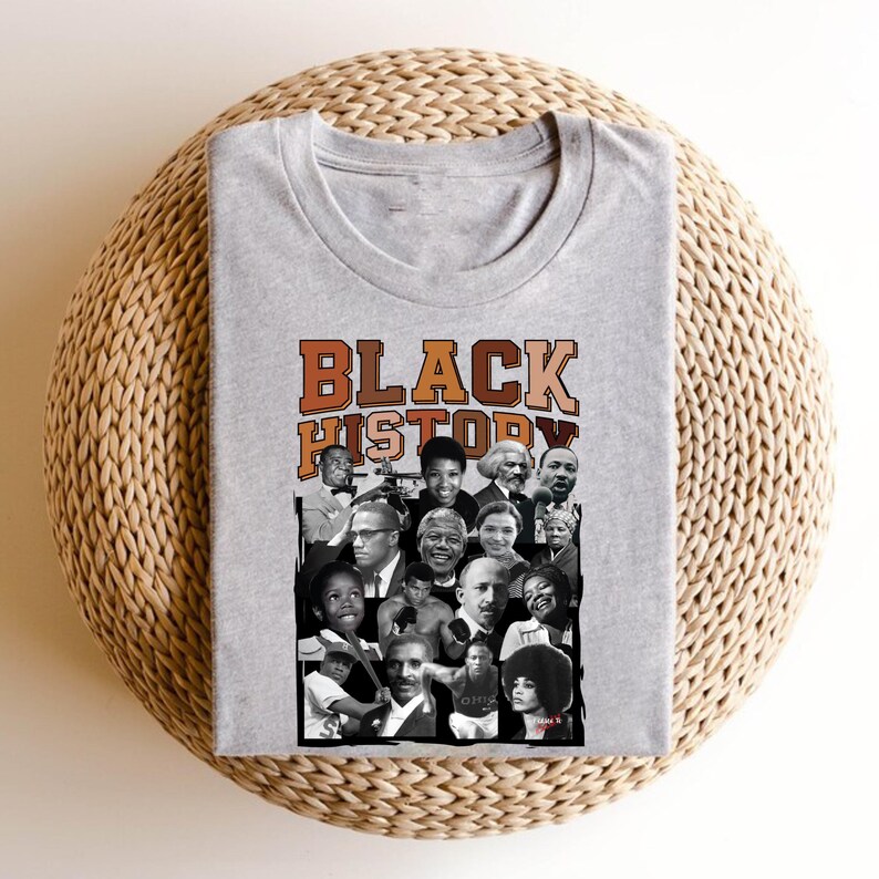 May include: A gray t-shirt with a collage of black and white photos of prominent African Americans. The text "BLACK HISTORY" is printed in orange, brown, and black letters across the top of the collage.