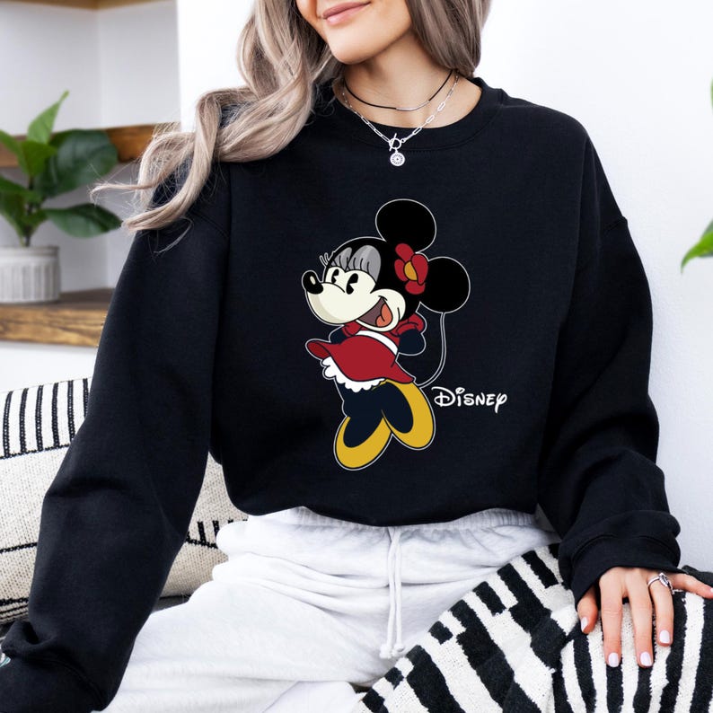 May include: Black sweatshirt with a cartoon image of Minnie Mouse in a red dress and a yellow bow. The text "DISNEY" is printed on the bottom right corner of the sweatshirt.