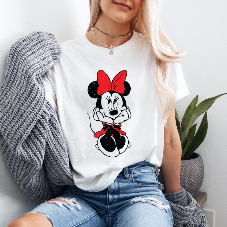 May include: White t-shirt with a black and white image of Minnie Mouse wearing a red bow. The image has a distressed look.