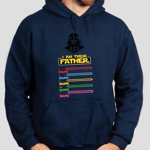 Pu&ograve; includere: Felpa con cappuccio blu navy con grafica di Darth Vader e la scritta "I AM THEIR FATHER". Sotto, spade laser colorate con la parola "NAME" sopra. Un capo d'abbigliamento a tema.