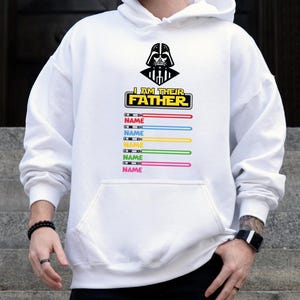 Pu&ograve; includere: Felpa con cappuccio bianca con una grafica di Darth Vader e la scritta "I AM THEIR FATHER". Sotto, disegni di spade laser colorate con la parola "NAME" stampata su ciascuna. La felpa ha una tasca frontale.
