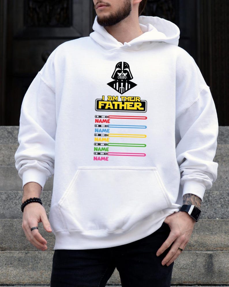 Pu&ograve; includere: Felpa con cappuccio bianca con una grafica di Darth Vader e la scritta "I AM THEIR FATHER". Sotto, disegni di spade laser colorate con la parola "NAME" stampata su ciascuna. La felpa ha una tasca frontale.