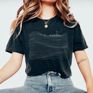 May include: Black t-shirt with a white line drawing of a boat on the ocean. The design features horizontal lines representing waves. The shirt is a dark charcoal color and has a vintage, worn look.