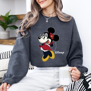 May include: A dark gray sweatshirt with a cartoon image of Minnie Mouse wearing a red dress and a yellow bow. The text "Disney" is printed below the image.