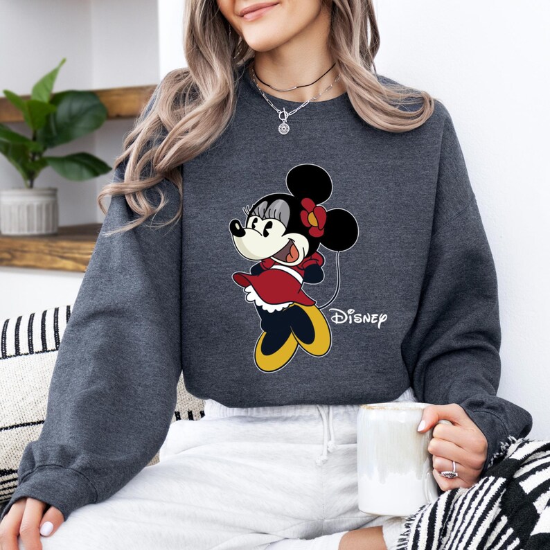 May include: A dark gray sweatshirt with a cartoon image of Minnie Mouse wearing a red dress and a yellow bow. The text "Disney" is printed below the image.