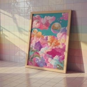May include: A framed art print featuring a vibrant, surreal landscape. The artwork depicts colorful clouds in shades of pink, orange, purple, and blue, with celestial bodies and palm fronds. The frame is made of light-colored wood.