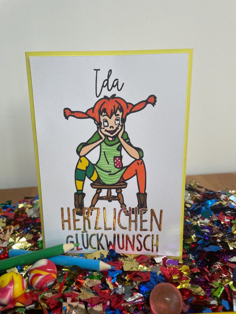 Puede incluir: Una tarjeta de felicitaci&oacute;n con una ilustraci&oacute;n de dibujos animados de una ni&ntilde;a con cabello rojo y un vestido verde. La tarjeta dice "Ida" y "Herzlichen Gl&uuml;ckwunsch", que se traduce como "Felicidades".
