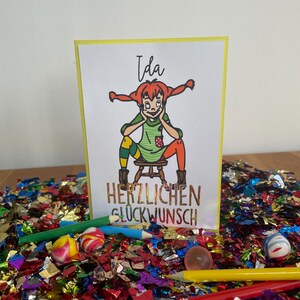 Puede incluir: Una tarjeta amarilla con una ilustraci&oacute;n de dibujos animados de una ni&ntilde;a con cabello rojo y un vestido verde. El texto "Ida" est&aacute; en la parte superior de la tarjeta y "HERZLICHEN GL&Uuml;CKWUNSCH" est&aacute; en la parte inferior.