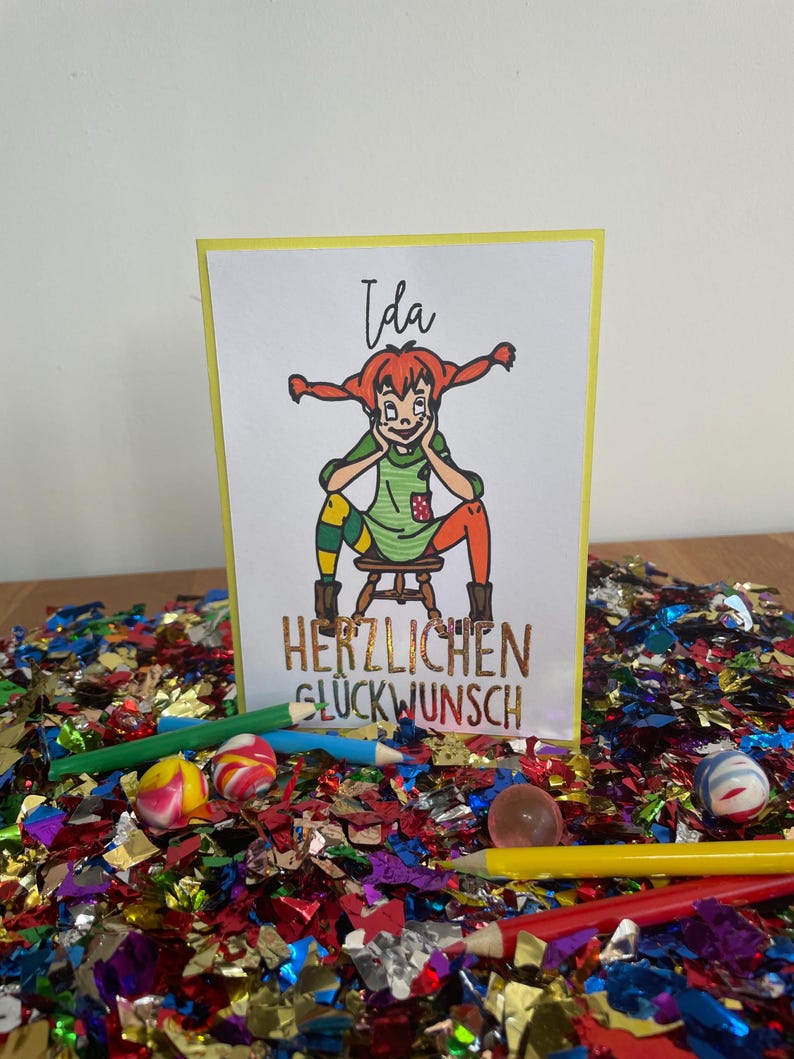 Puede incluir: Una tarjeta amarilla con una ilustraci&oacute;n de dibujos animados de una ni&ntilde;a con cabello rojo y un vestido verde. El texto "Ida" est&aacute; en la parte superior de la tarjeta y "HERZLICHEN GL&Uuml;CKWUNSCH" est&aacute; en la parte inferior.