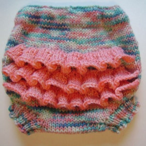 May include: Hand-knitted baby bloomers in a mix of pastel colors, including pink, blue, and green. The bloomers feature a ruffled design in a solid pink color across the front. The soft, textured knitwear is designed for comfort.